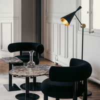 Black upholstered chairs and marble tables with sleek, modern patterns, complemented by a stylish black and gold lamp.