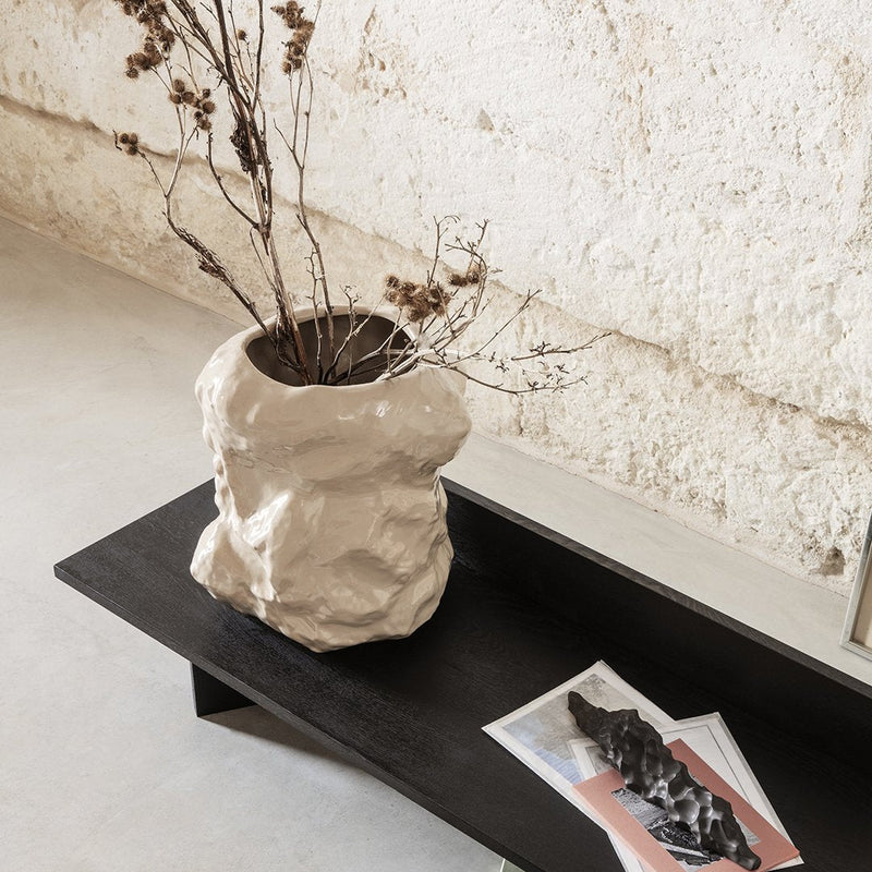 Textured beige vase with dried branches on a sleek black table, set against a neutral wall. Perfect for modern decor.