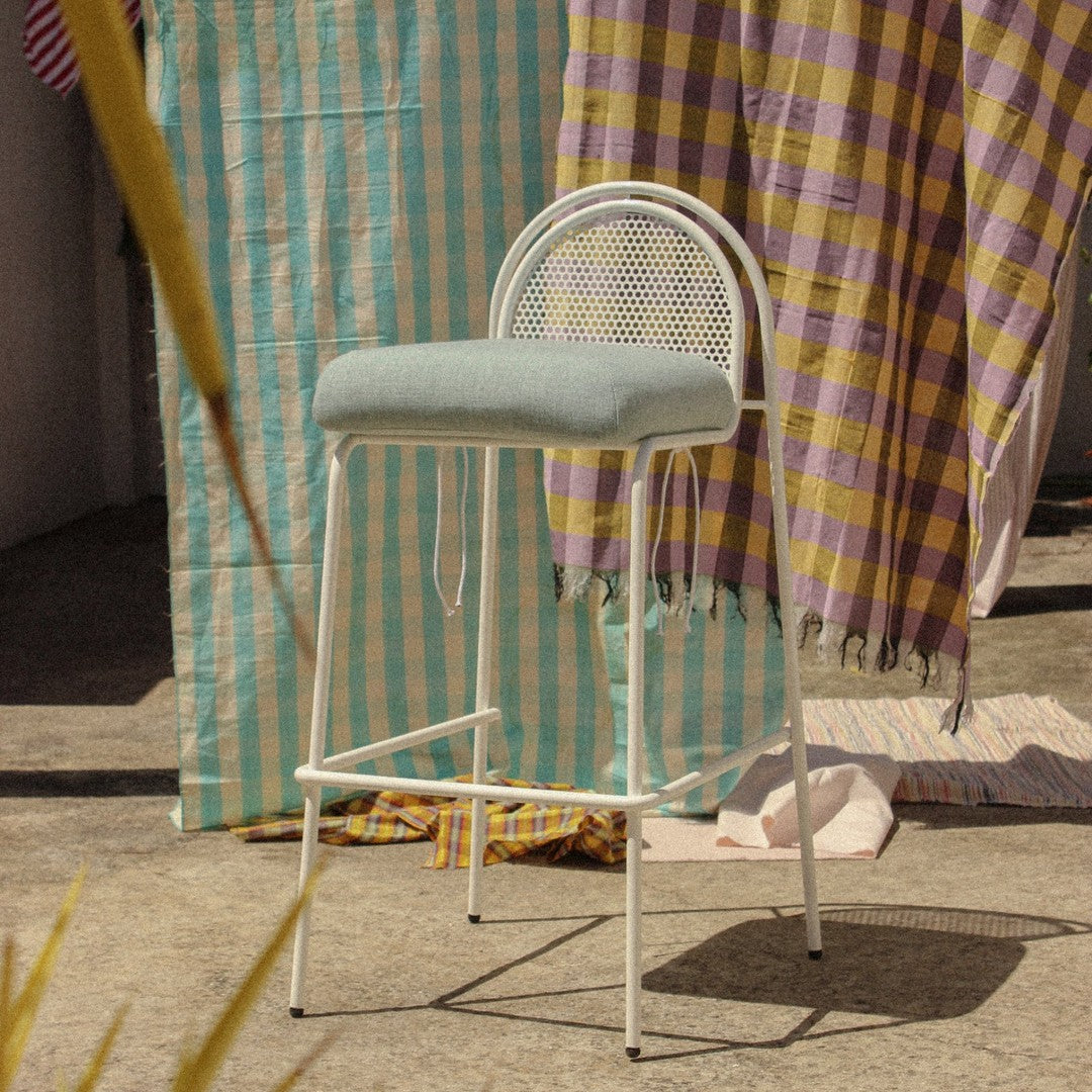 Light blue upholstered stool with a patterned backdrop of yellow and purple checkered fabrics.