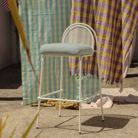 Light blue upholstered stool with a patterned backdrop of yellow and purple checkered fabrics.