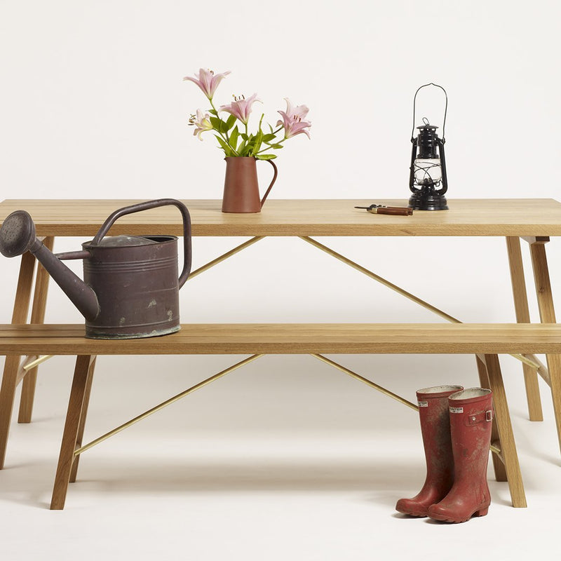 Natural wood table with gold accents, paired with a gray watering can, red boots, and pink flower arrangement.