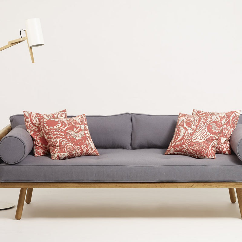 Gray sofa with vibrant red paisley-patterned pillows, styled with a modern wooden base and a minimalist lamp.