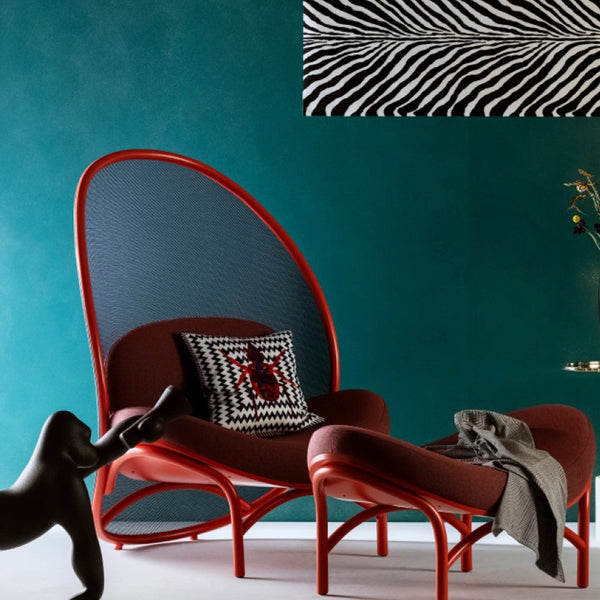 Red mid-century modern chair and ottoman with black woven accents and a black and white zebra stripe pillow against a turquoise wall.