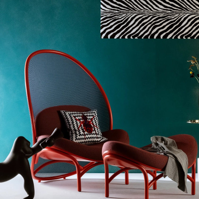 Red mid-century modern chair and ottoman with black woven accents and a black and white zebra stripe pillow against a turquoise wall.
