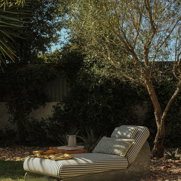 Chic outdoor lounge chair with white and gray stripes, complemented by a textured pillow and warm wooden accents.