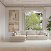 Stylish beige sectional sofa with soft textures, complemented by a light rug and neutral wall art in a bright, airy room.