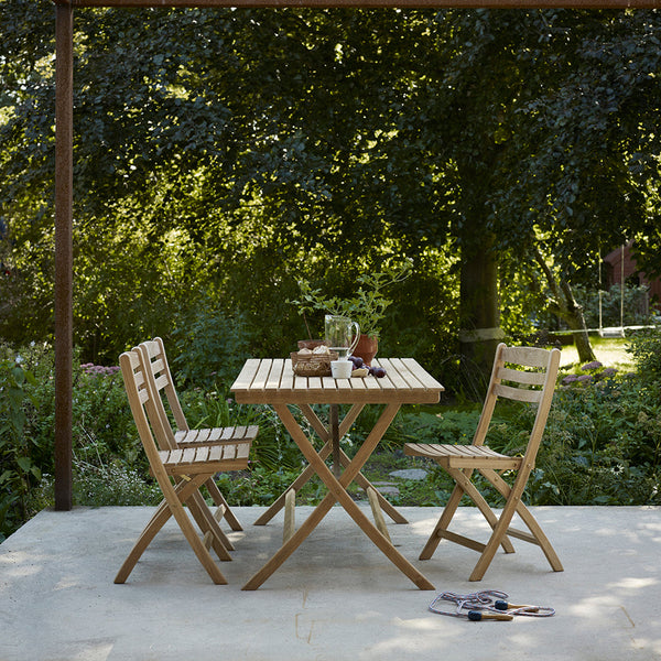 Natural wood folding table and chairs with a slatted design, set against a green garden backdrop.