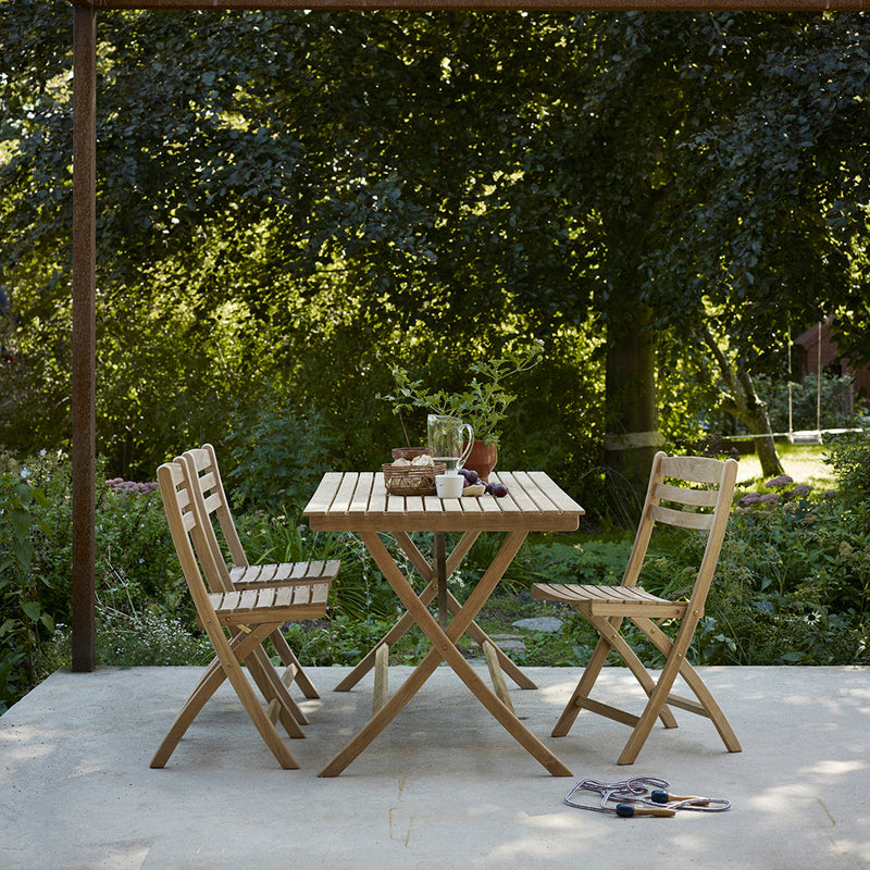 Natural wood folding table and chairs with a slatted design, set against a green garden backdrop.