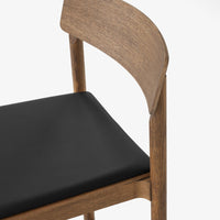 "Wooden chair with a natural finish and a sleek black cushion, featuring smooth lines and a modern aesthetic."
