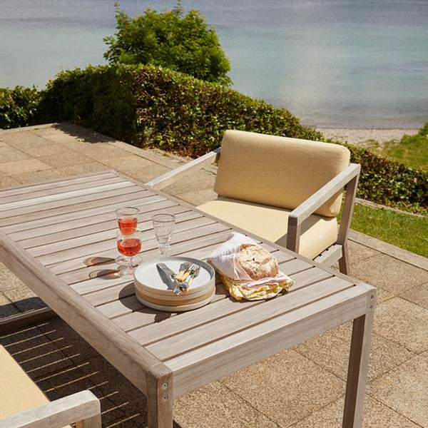 Light beige cushions on modern wooden patio furniture, set against a serene blue ocean backdrop.