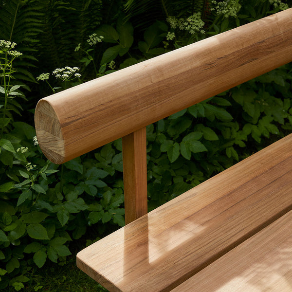 Light brown wooden bench with a smooth finish, featuring natural wood grain patterns against a lush green background.