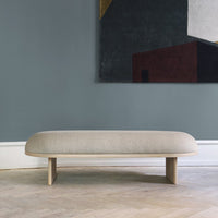 Light beige minimalist bench with smooth curves against a muted gray wall and abstract art featuring rich colors.