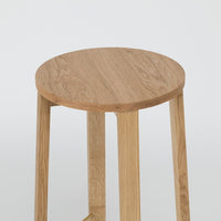Natural wood round stool with a light oak finish and smooth grain pattern, featuring simple, minimalist design.