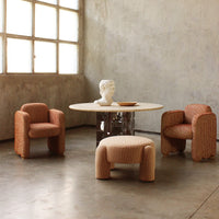 "Textured peach armchairs and round table with a smooth surface, set against a minimalist concrete backdrop."