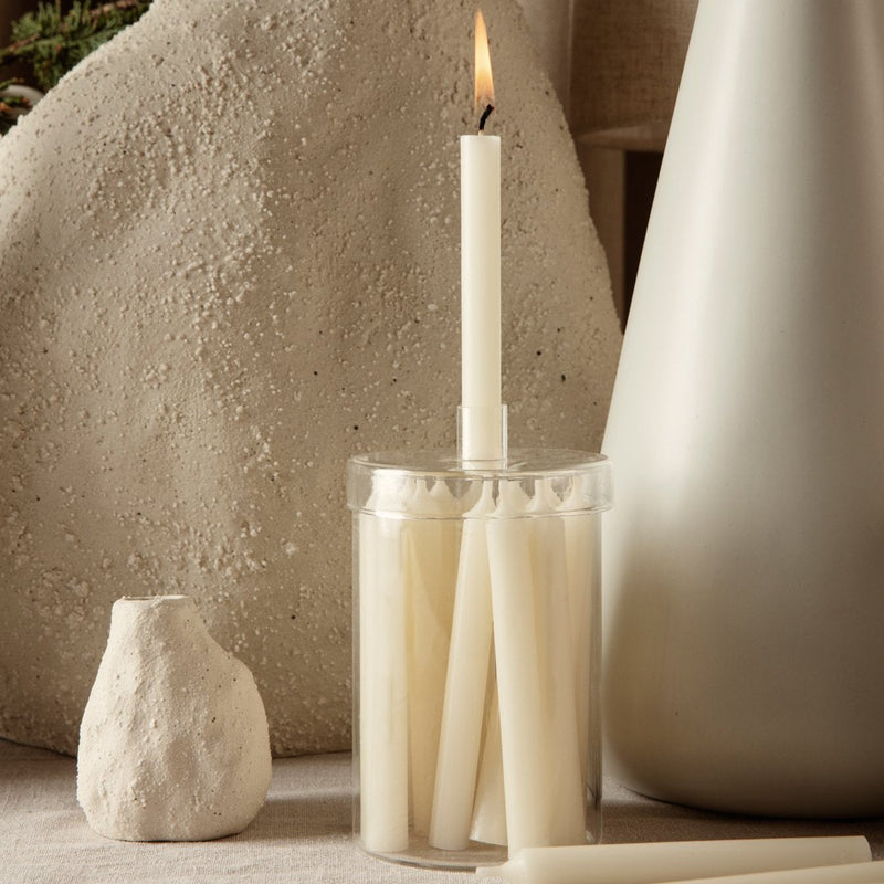 Cream-colored taper candles in a clear holder against neutral backgrounds, featuring soft textures and minimalist design.