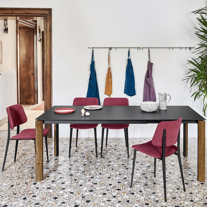 Black dining table with burgundy chairs, featuring patterned floor tiles in shades of gray and blue.