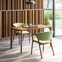Wooden table with natural finish and two mint green chairs, set against a backdrop of warm wood paneling and geometric floor patterns.