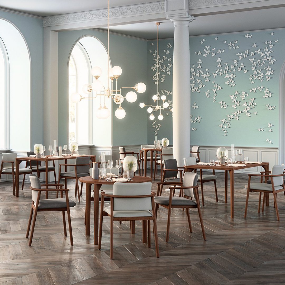Elegant dining room with light blue walls, warm wood textures, and white floral wall art. Modern chairs in neutral tones.