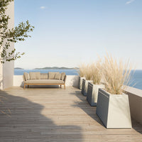 Beige outdoor sofa with light gray planters and natural wood decking, accented by green plants against a blue sky.