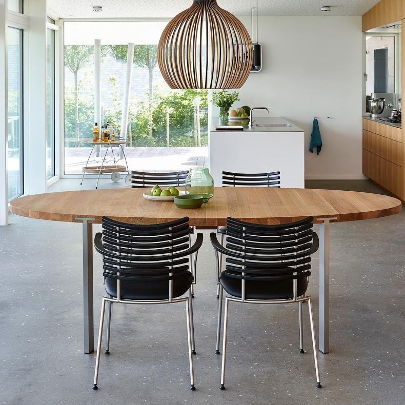 Natural wood dining table with sleek black striped chairs and a modern wooden pendant light, set in a bright, airy interior.