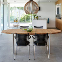Natural wood dining table with sleek black striped chairs and a modern wooden pendant light, set in a bright, airy interior.