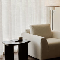 Beige textured armchair with muted stripes and neutral light-filtering curtains in soft, airy tones.