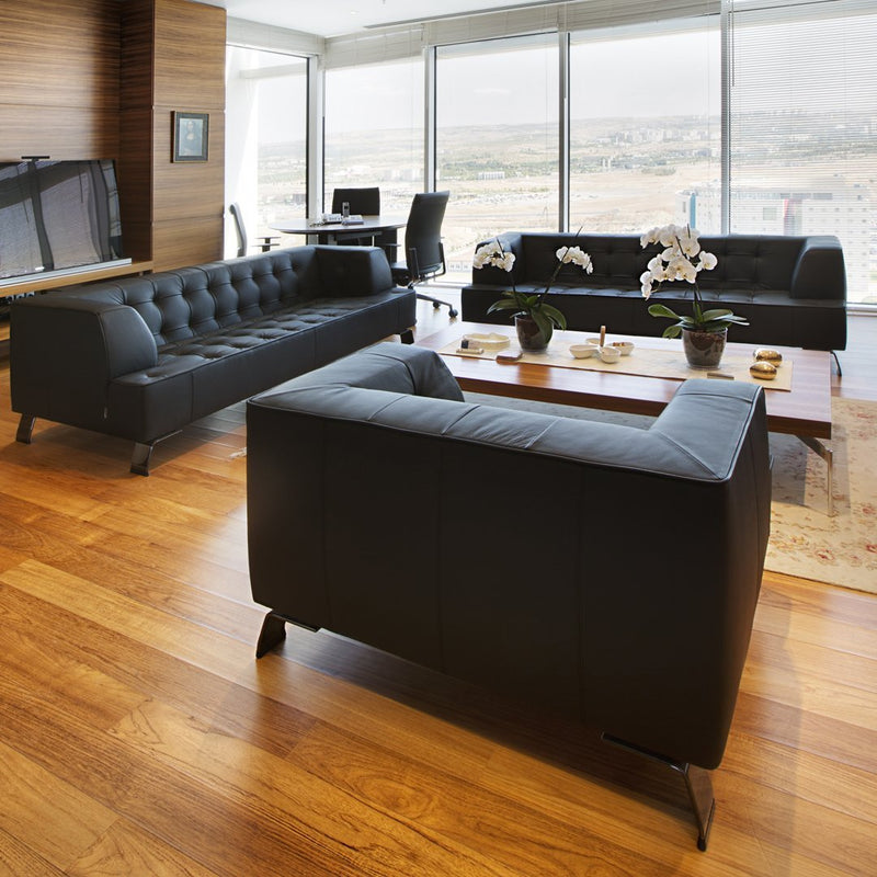 Black tufted sofas with sleek lines, set against warm wooden flooring and modern decor.