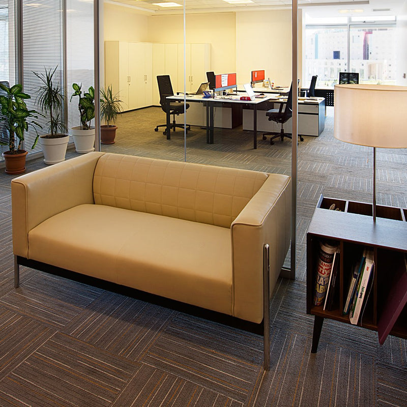 Beige sofa with a minimalist design, complemented by a modern, wooden side table and a patterned gray carpet.