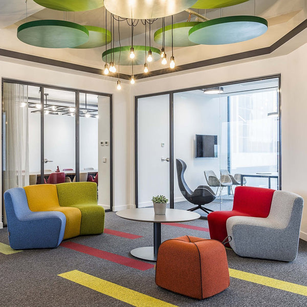 Vibrant armchairs in yellow, green, red, and blue, complemented by a round table and colorful area rug patterns.