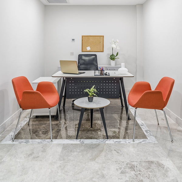Modern office space featuring orange chairs and a minimalist black desk on a light marble floor, accented by green plants.