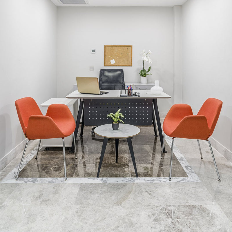 Modern office space featuring orange chairs and a minimalist black desk on a light marble floor, accented by green plants.