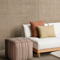 White sofa with striped pouf in earthy tones; orange and green decorative cushions add a pop of color.