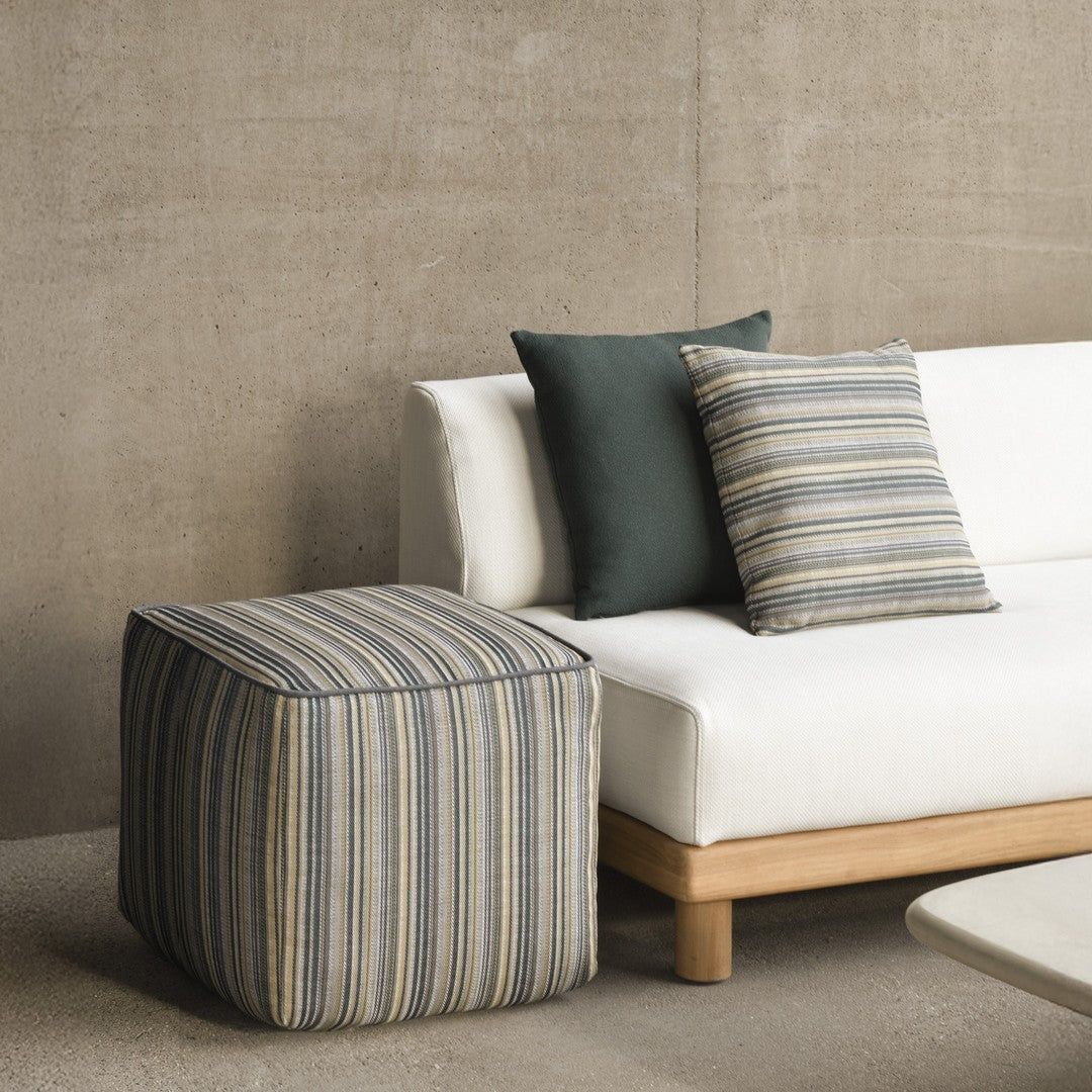Blue and beige striped pouf beside dark green and striped pillows on a modern white sofa. Chic, contemporary design.