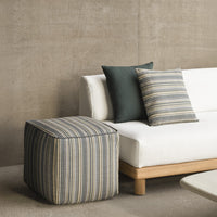 Blue and beige striped pouf beside dark green and striped pillows on a modern white sofa. Chic, contemporary design.