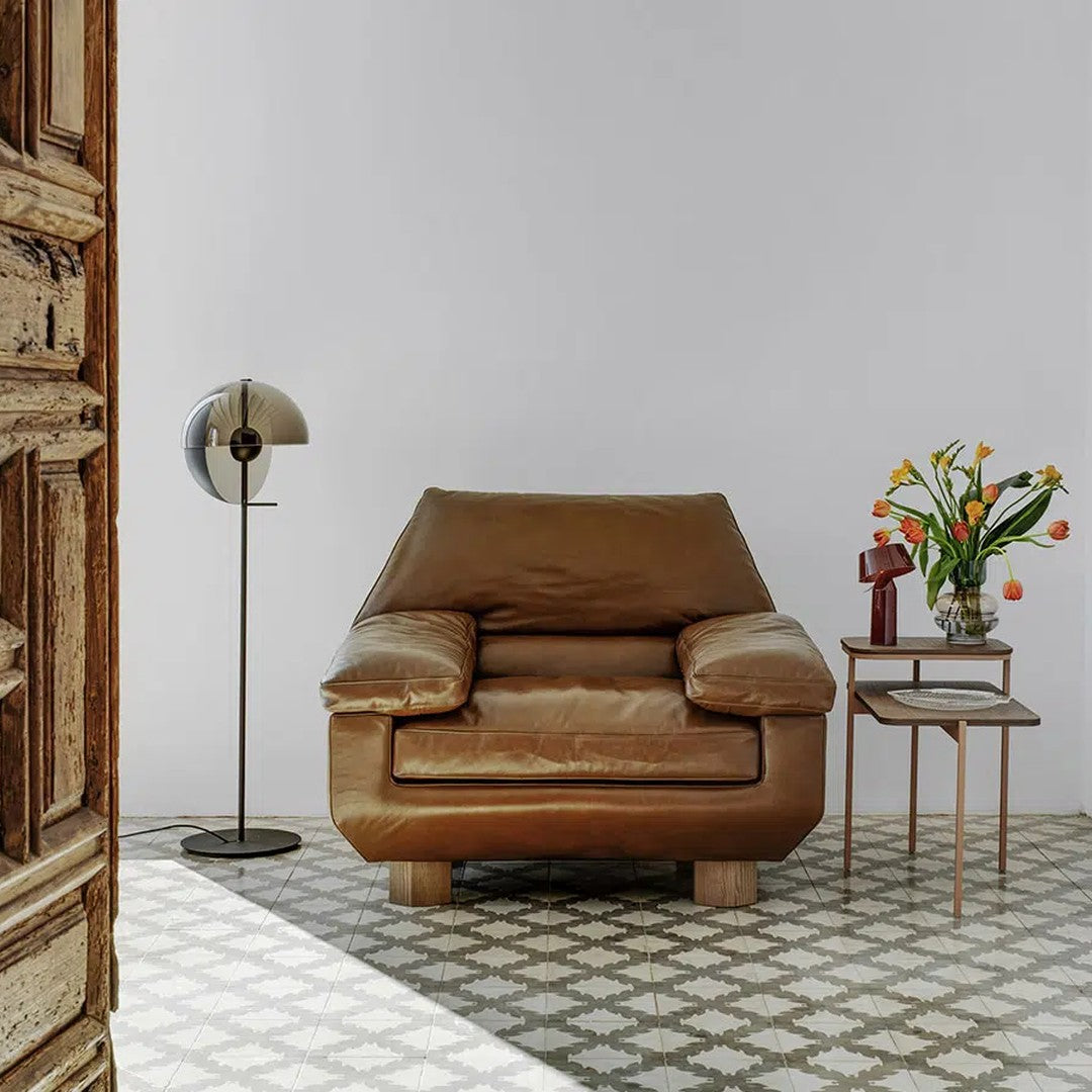 Brown leather armchair on patterned gray floor with white and green accents. Stylish decor in minimalist setting.