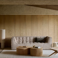 Beige textured sofa with subtle diagonal patterns, accompanied by light wooden coffee tables in a warm, neutral-toned room.
