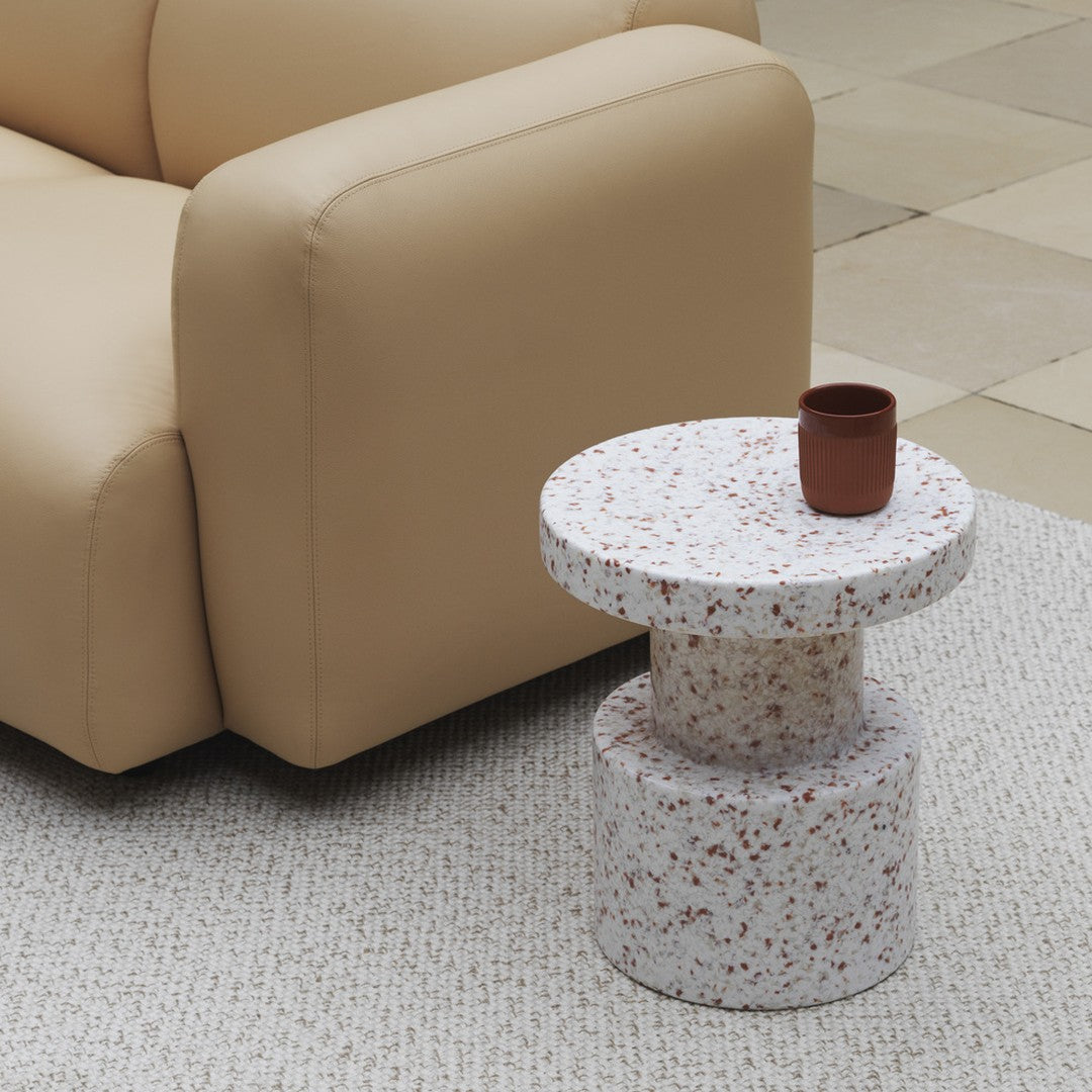 "Round terrazzo side table in white with red speckles, paired with a minimalistic brown ceramic cup."