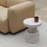 "Round terrazzo side table in white with red speckles, paired with a minimalistic brown ceramic cup."