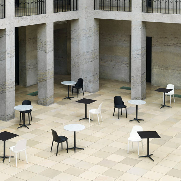 Modern outdoor seating with black, white, and gray tables and chairs on a patterned stone floor in an architectural space.
