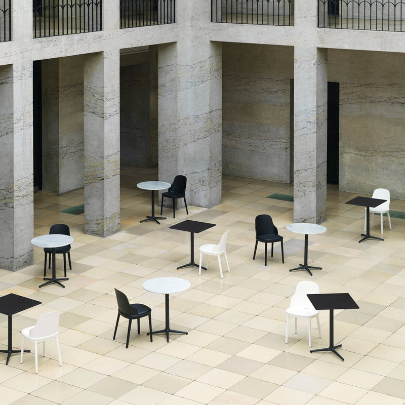 Modern outdoor seating with black, white, and gray tables and chairs on a patterned stone floor in an architectural space.