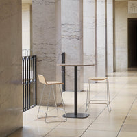 Minimalist round table with a black base and light wood chairs, set against a sleek marble pattern backdrop.