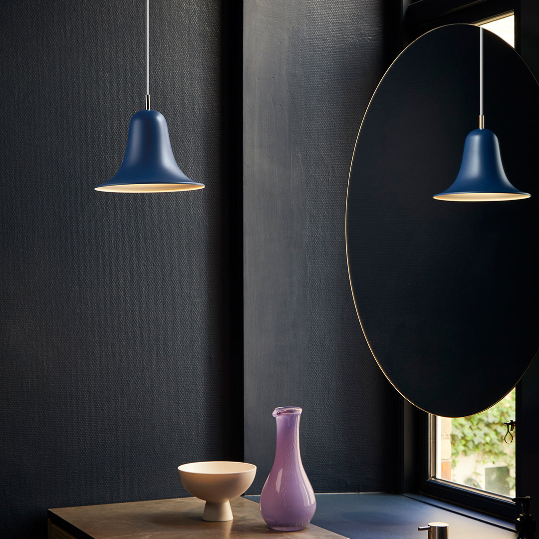 Navy blue pendant lamp with a smooth finish, complemented by a round mirror and soft purple vase on a wood table.