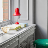 Red bell lamp on a light gray surface with stacked white and blue books, accented by a green stool and decorative shell.