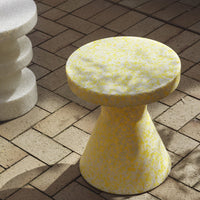 Yellow speckled stool with a geometric conical shape, set against a textured brick floor.