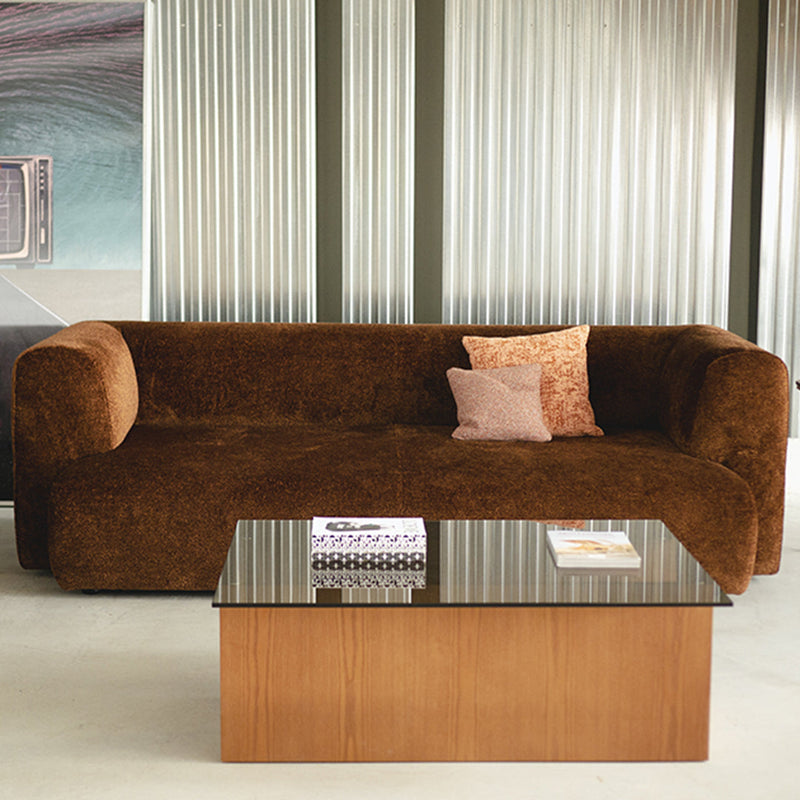 Brown textured sofa with a light pink accent pillow, paired with a sleek wooden coffee table and patterned magazine.