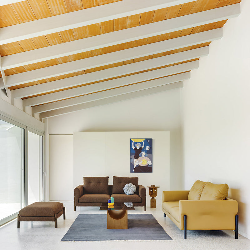 Modern living room with brown and mustard sofas, geometric-patterned rug, and light wooden beams on the ceiling.