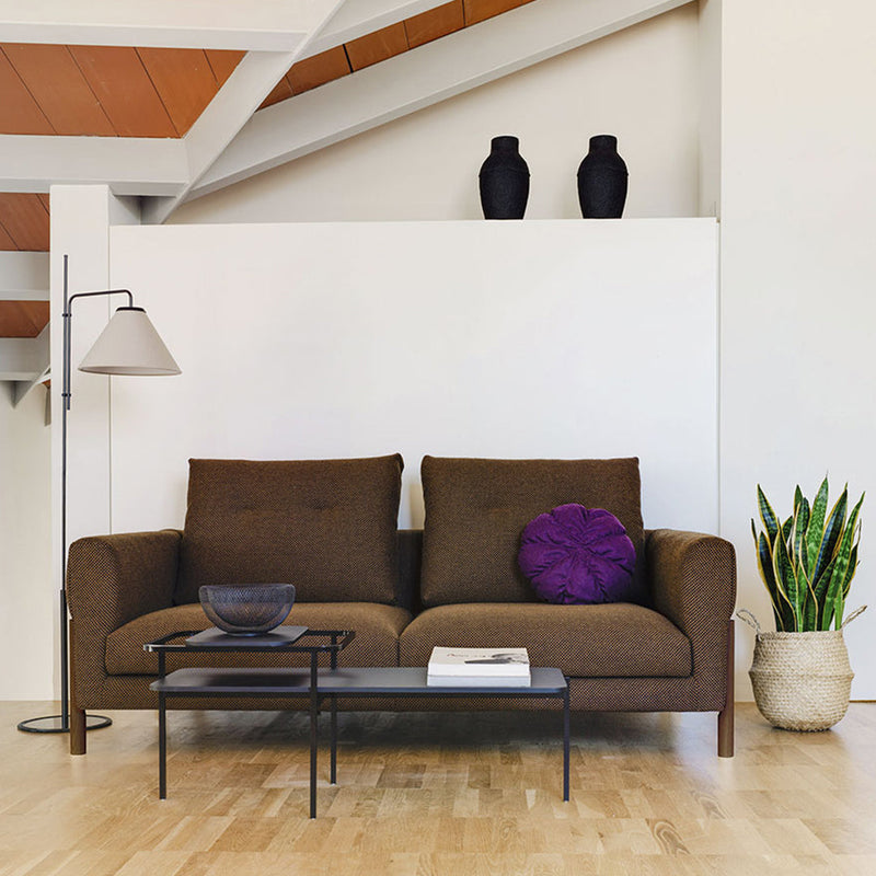 Brown sofa with purple accent pillow, black table, and neutral decor, featuring a warm wood floor and greenery.