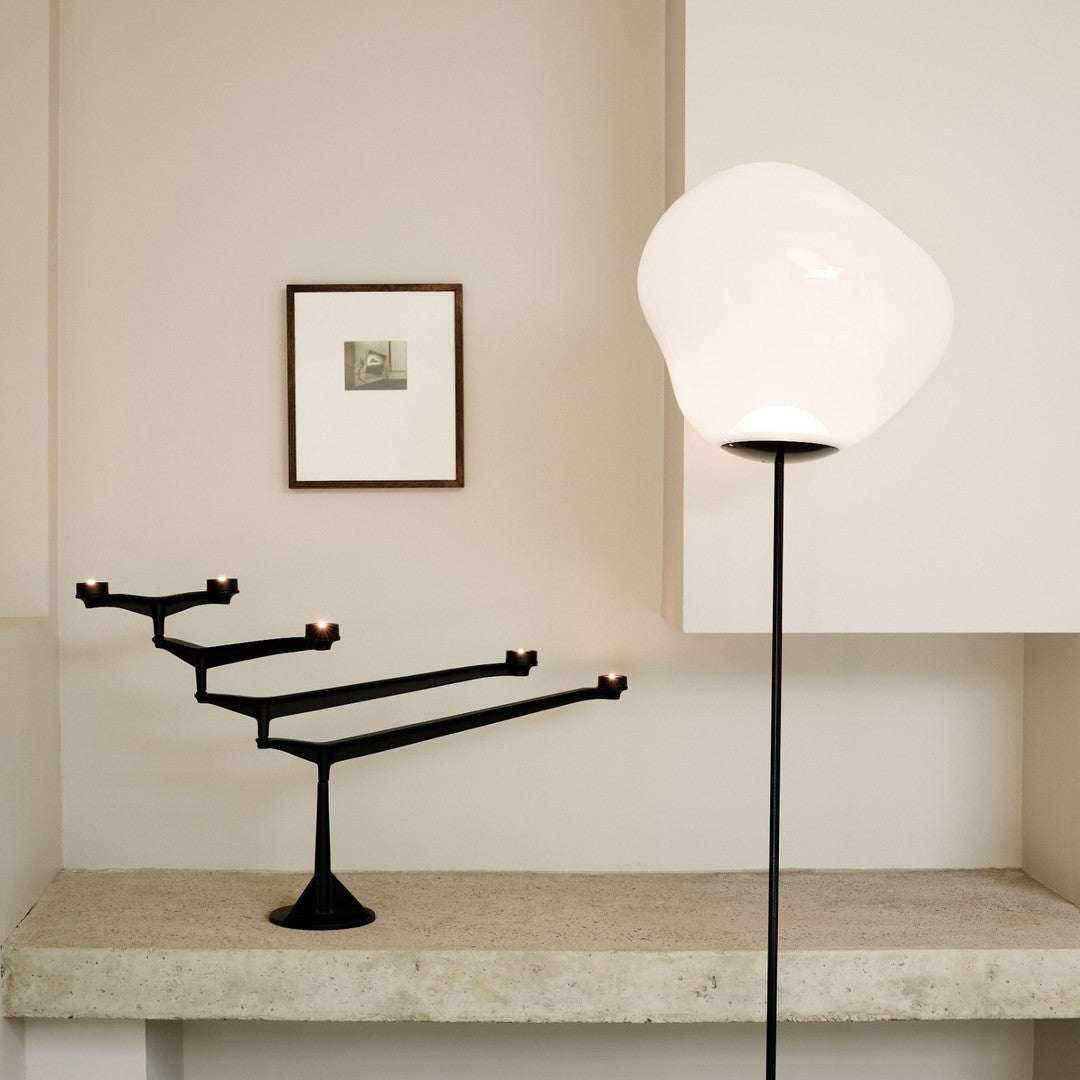 "Modern black candle holder with minimalistic design against a neutral wall, complemented by a soft white lamp."