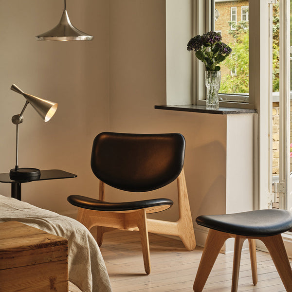 Sleek black leather chair with natural wood legs, complemented by minimalist light fixtures and neutral room tones.