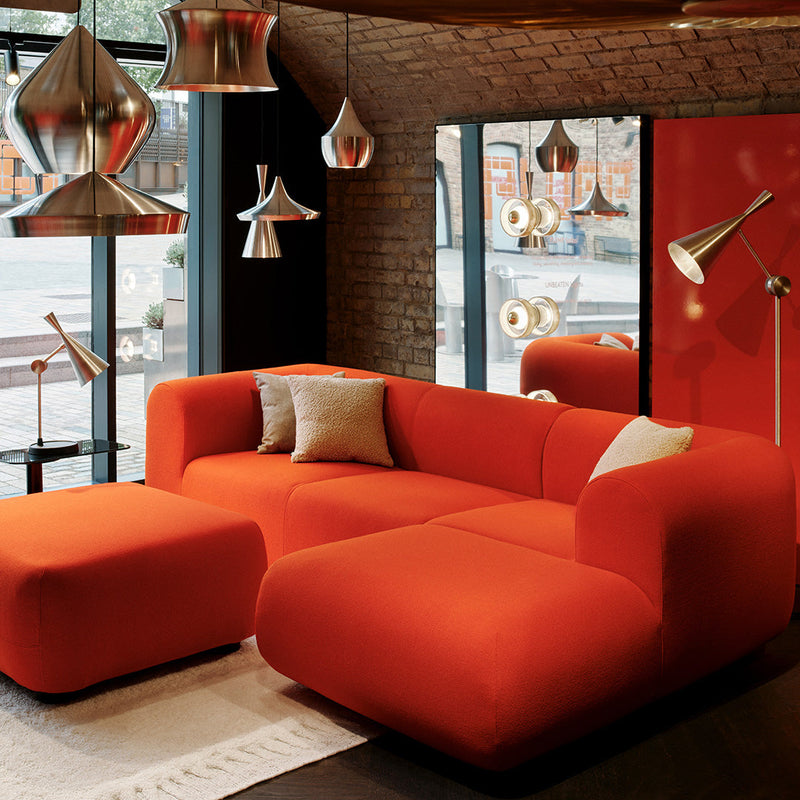 Vibrant orange modern sectional sofa with matching ottoman, featuring smooth, minimalist shapes and a contemporary design.